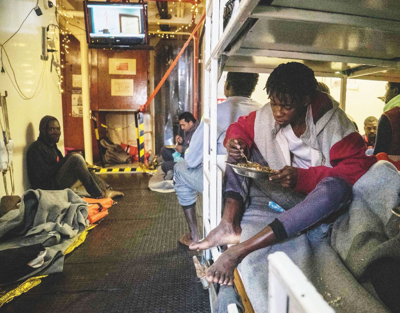 Rescued migrants eat a hot meal onboard the Dutch-flagged rescue vessel Sea Watch 3 on January 5, 2019, sailing the Mediterranean about 3 nautical miles off Malta's coast, a day after Mediterranea and Sea-Watch launched two boats to deliver supplies, including fresh water. - Thirty-two migrants, including children and teenagers rescued off Malta by a Sea-Watch rescue boat on December 22, 2018 remain at sea after being denied entry to European ports. The boat was given permission by Malta on January 3 to shelter off its coast due to a storm and fierce winds, but not to land. (Photo by FEDERICO SCOPPA / AFP)