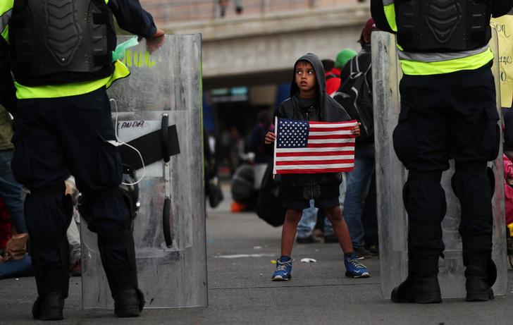 Michael Joel Miranda, an eight-year-old migrant boy from Honduras, part of a caravan of thousands from Central America trying to reach the United States, holds a U.S flag in front of Mexican riot police at the El Chaparral port of entry border crossing between Mexico and the United States, in Tijuana, Mexico, November 22, 2018. REUTERS/Hannah McKay